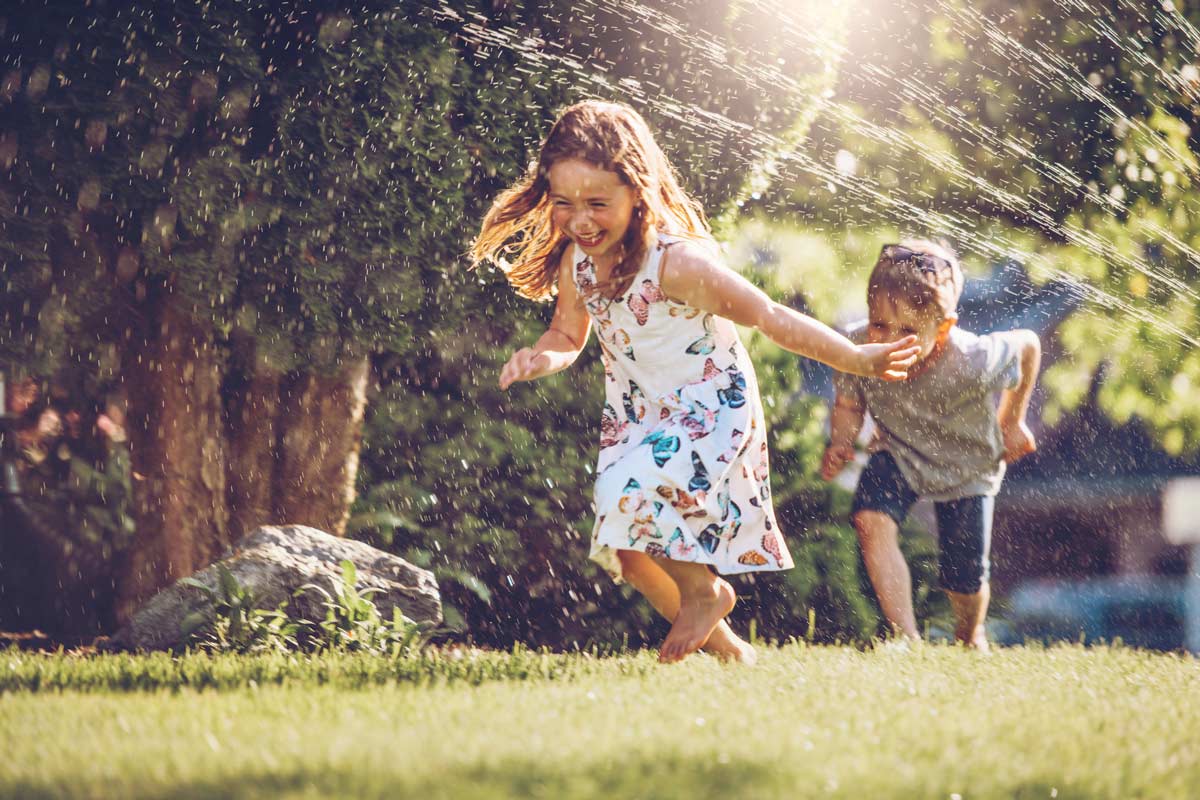 Kids running through a sprinkler on a lawn in summer